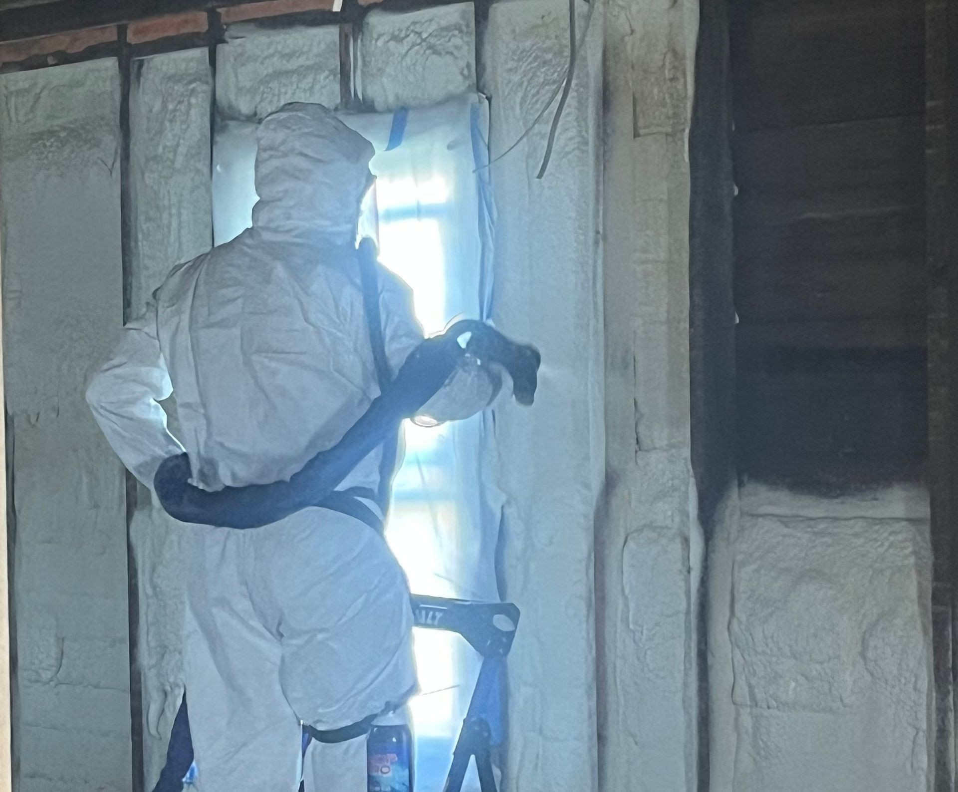 Worker spraying polyurethane foam for insulating wooden frame house.