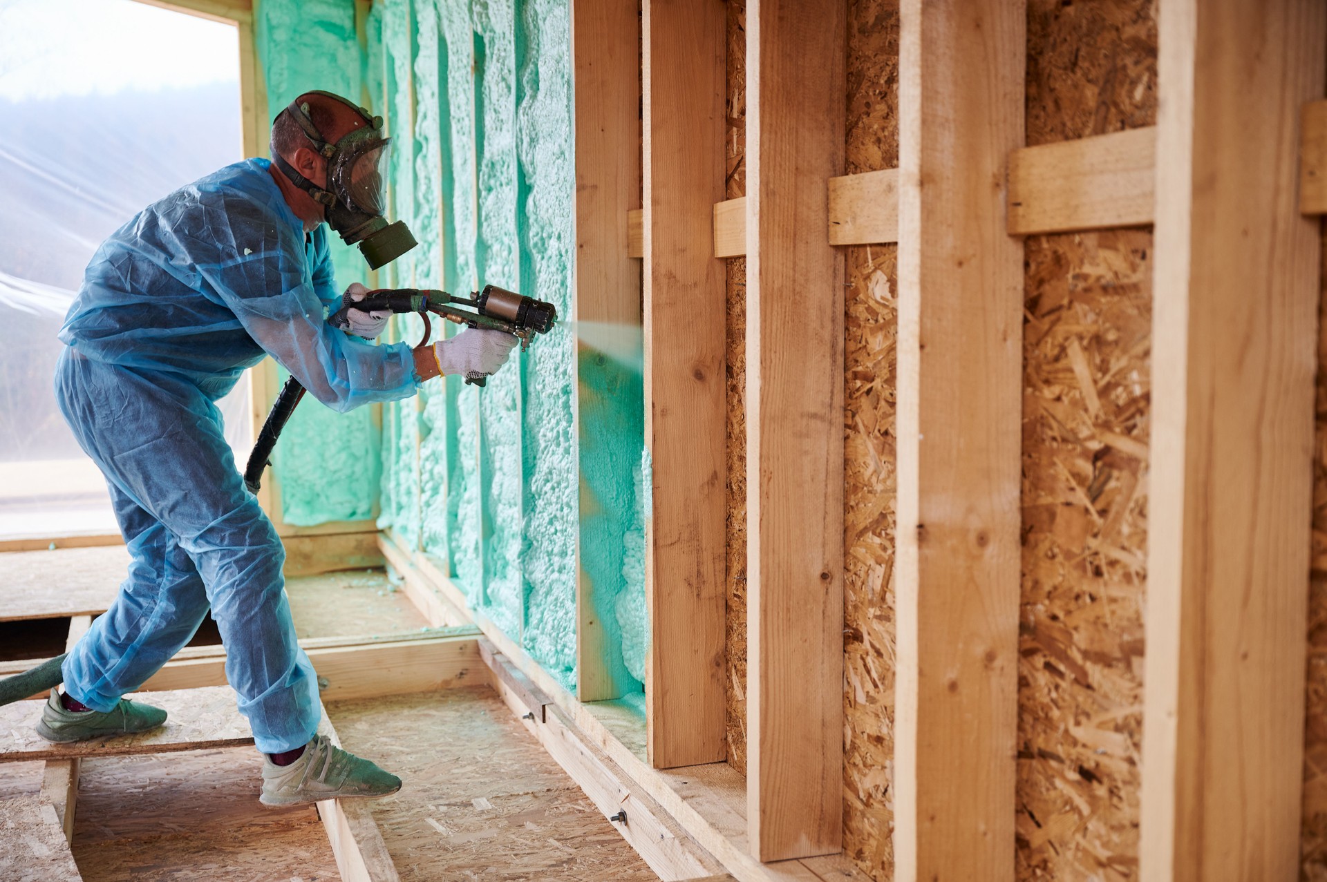 Worker spraying polyurethane foam for insulating wooden frame house.